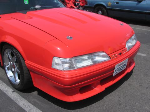 1996 Ford C-350 (Centurion Conversions) - The front of a red Ford Mustang is visible, with a blue police car in the background.