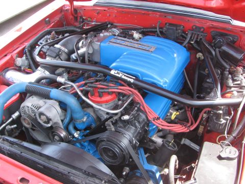 1996 Ford C-350 (Centurion Conversions) - Close-up view of a modified engine bay bright blue valve covers and a black strut tower brace.