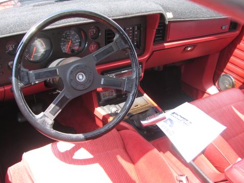 1996 Ford C-350 (Centurion Conversions) - Car interior with a steering wheel, dashboard gauges, and red seats. A document is visible on the passenger seat.