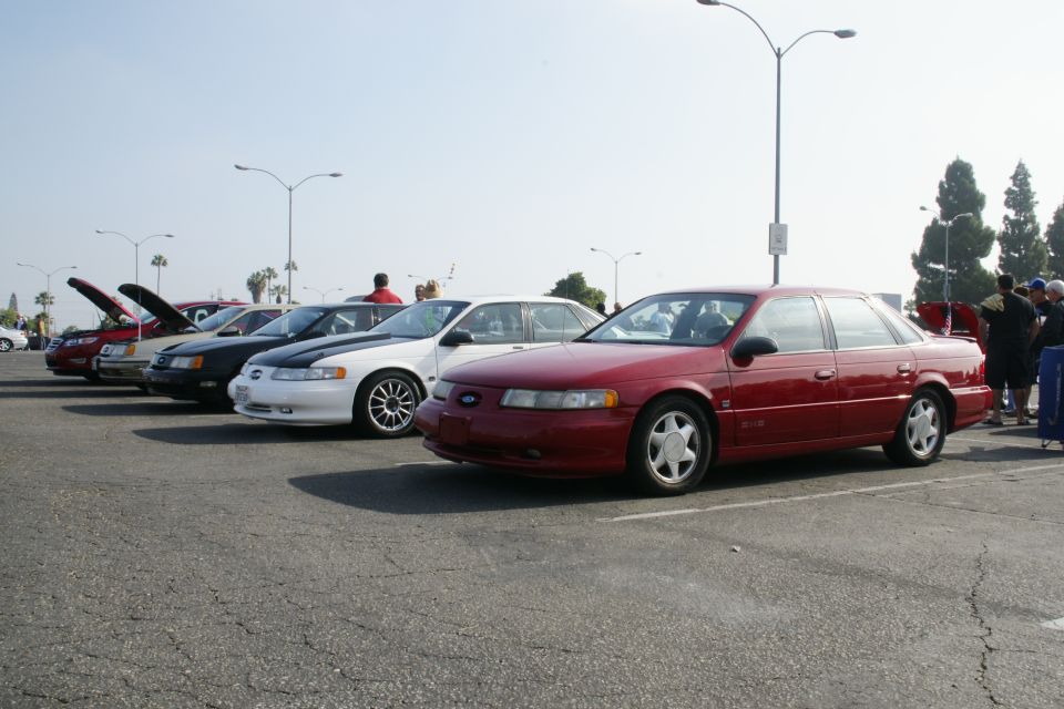 Red 1996 Ford Taurus sedan parked in a lot, front quarter view. Other cars are lined up behind it