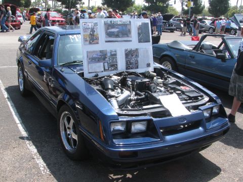 1996 Ford C-350 (Centurion Conversions) - A blue Ford Mustang is displayed with its hood open, revealing the engine and a presentation board.