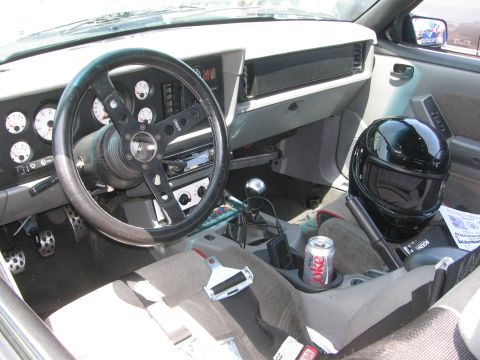 1996 Ford C-350 (Centurion Conversions) - The interior of a vehicle features a racing steering wheel, custom gauges, a black helmet, and a can of Coca-Cola in the cup holder.