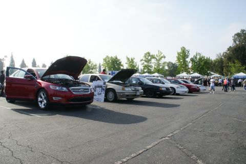 1992 Ford Taurus - A red sedan is displayed with its hood and driver's door open at an outdoor car show.