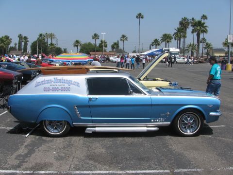 1996 Ford C-350 (Centurion Conversions) - Modified Ford Mustang station wagon with surfboard and rack, parked at an outdoor event with other vehicles and people.
