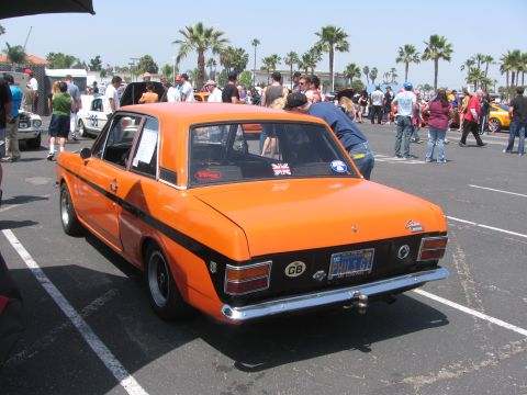 1996 Ford C-350 (Centurion Conversions) - Orange coupe with black stripe, rear view, parked in lot with people.
