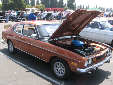 1996 Ford C-350 (Centurion Conversions) - A brown 1974 Ford Capri coupe is displayed with its hood open at a car show, with other vehicles in the background.