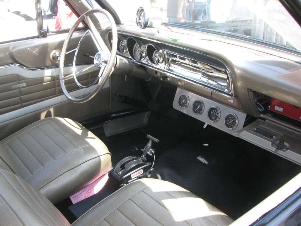 Interior view of a classic car with a chrome steering wheel, tan seats, and aftermarket gauges