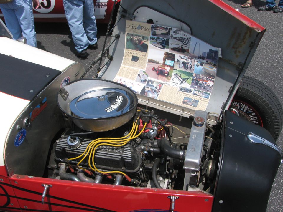 Hot rod engine bay with newspaper clippings taped inside the hood. Engine has yellow spark plug wires