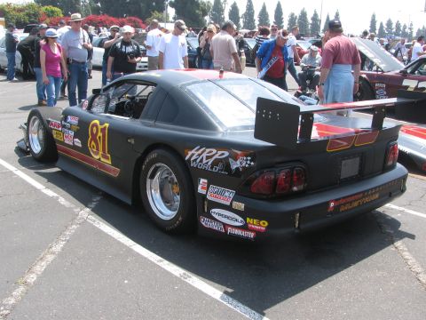 1996 Ford C-350 (Centurion Conversions) - A black race car with racing decals and a large rear spoiler is parked in a lot with spectators.