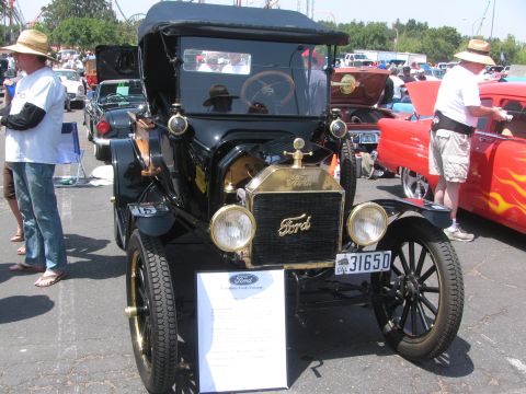 1996 Ford C-350 (Centurion Conversions) - A vintage black Ford Model T is displayed at an outdoor event with other vehicles and attendees.
