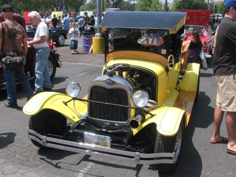 1996 Ford C-350 (Centurion Conversions) - A yellow 1928 Ford Model A pickup truck is parked at an outdoor event with other vehicles and people.