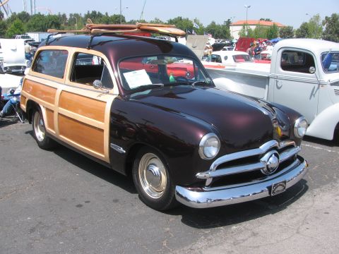 1996 Ford C-350 (Centurion Conversions) - A classic woodie station wagon is parked at an outdoor event, with surfboards on its roof rack.