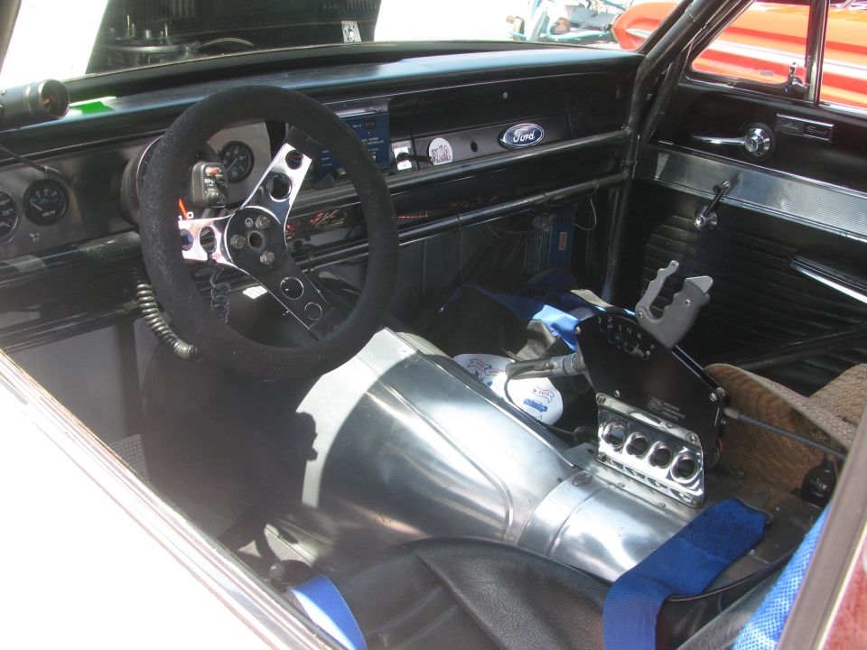 Custom race car interior with aftermarket steering wheel, floor shifter, and gauges. Ford logo visible on dashboard