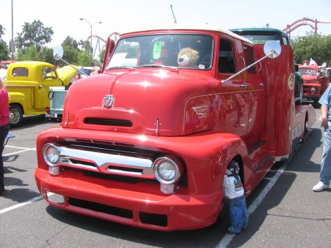 1996 Ford C-350 (Centurion Conversions) - A bright red tow truck is parked at an outdoor event, with a child hiding near its front wheel.