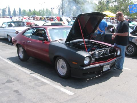 1996 Ford C-350 (Centurion Conversions) - A man inspects a modified Ford Pinto with its hood up, parked in a lot with other vehicles.