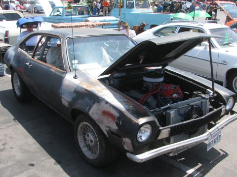 1996 Ford C-350 (Centurion Conversions) - A weathered Ford Pinto with its hood up, revealing the engine bay, sits among other vehicles at an outdoor gathering.