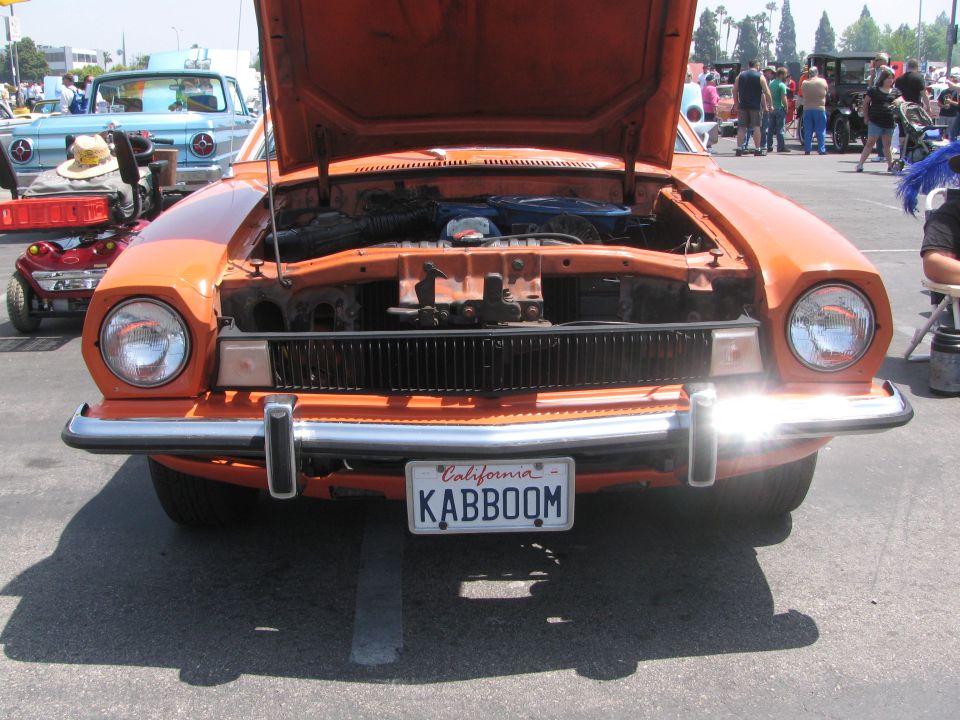 Orange car, hood open, showing engine bay. California license plate KABBOOM. Another car visible behind it