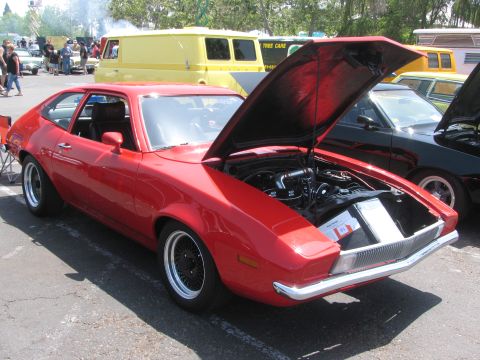 1996 Ford C-350 (Centurion Conversions) - A red coupe from the 1970s is displayed with its hood open, revealing the engine and a document placed in the engine bay.