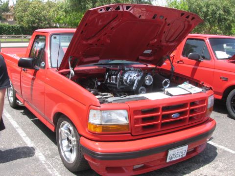 1996 Ford C-350 (Centurion Conversions) - Red pickup truck with hood open, displaying a supercharged engine. Another red truck is visible to the right.