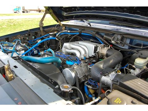 1994 Ford Bronco - The engine bay is filled with blue hoses and a silver intake manifold, with a truck visible in the background.