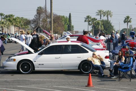 1992 Ford Taurus - A white sedan with its hood open is parked at an outdoor car show with people around.