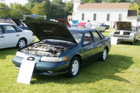1992 Ford Taurus - A dark green 1992 Ford Taurus SHO is displayed with its hood open at an outdoor car show.