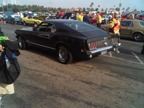 1986 Ford Bronco - A black 1969 Ford Mustang Mach 1 is parked at an outdoor car show, displaying its distinctive rear end and Cooper Cobra tires.