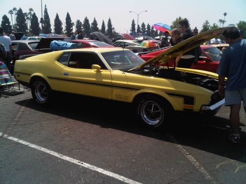 1986 Ford Bronco - A yellow 1971 Ford Mustang Mach 1 is displayed with its hood open at an outdoor car show.