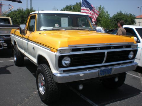 1979 Ford Bronco - This two-tone Ford pickup truck, possibly from 1975, is parked outdoors with an American flag in the background.