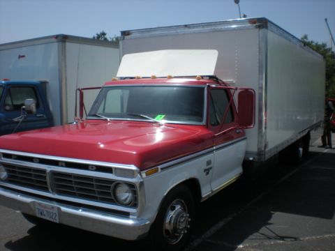 1979 Ford Bronco - A red and white Ford truck is parked next to a white box trailer, with another blue truck visible to the left.