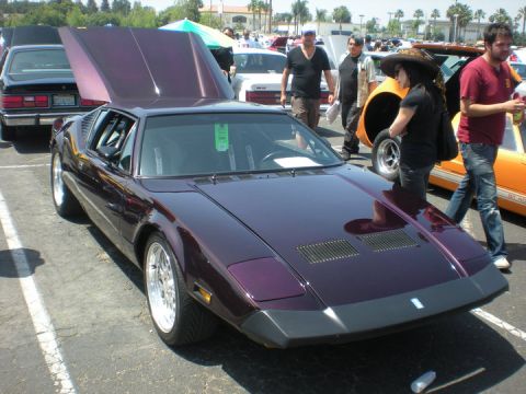 1979 Ford Bronco - A purple sports car with its hood open is displayed at an outdoor event, with other vehicles and people in the background.
