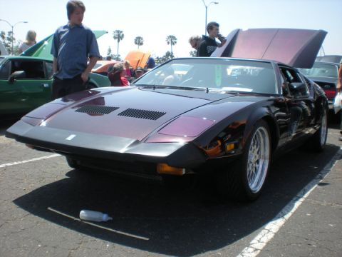 1979 Ford Bronco - A purple De Tomaso Pantera is displayed at a car show with other vehicles and people around.