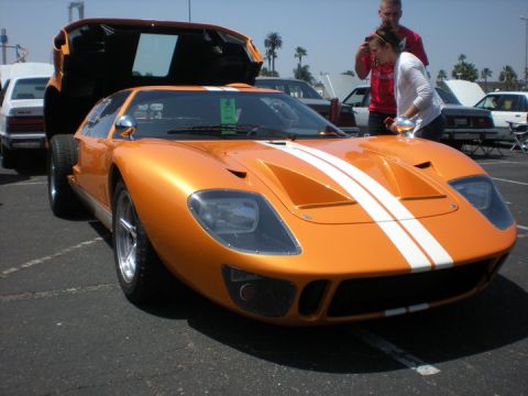 1979 Ford Bronco - An orange sports car with white stripes is parked outside with its hood open.