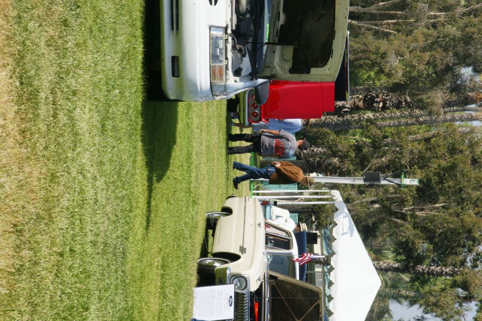 two old cars parked on grass, one with hood up, people looking at them