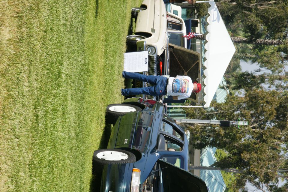 Dark green sedan, hood open, parked on grass next to a white tent. A person stands by the car