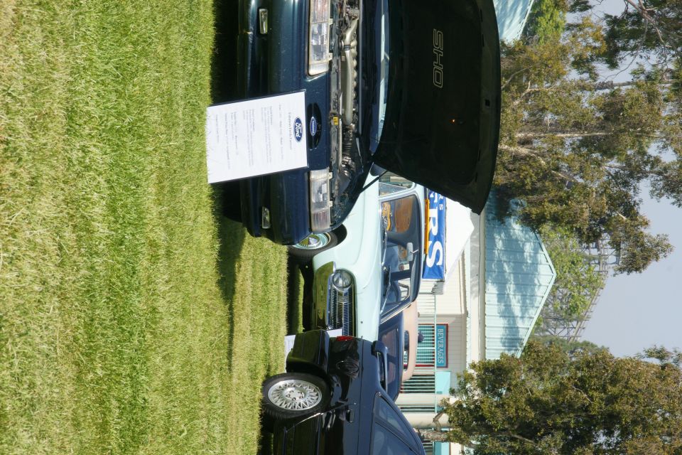 dark green 1992 Ford Taurus SHO with hood open, parked on grass next to a light blue car