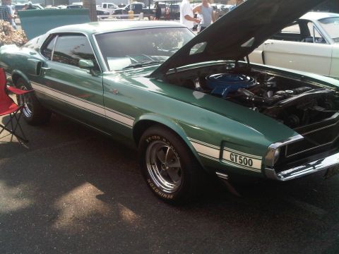 1986 Ford Bronco - A green 1969 Ford Mustang GT500 with its hood open is displayed at an outdoor event.