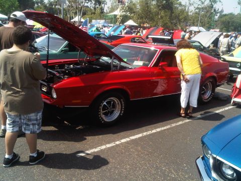 1986 Ford Bronco - A red 1971 Ford Mustang Mach 1 is displayed with its hood open at an outdoor car show, attracting onlookers.