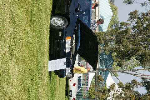 1992 Ford Taurus - A black sedan's hood is open at an outdoor car show, with people examining the engine bay.