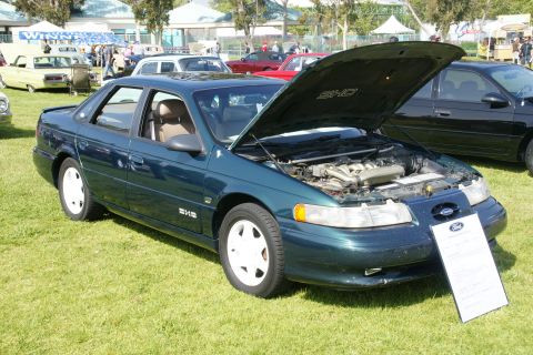 1992 Ford Taurus - A dark green 1992 Ford Taurus SHO is displayed with its hood open, revealing the engine, at an outdoor car show.