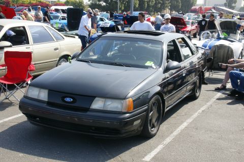 1992 Ford Taurus - A dark gray Ford Taurus is parked at an outdoor car show, with other vehicles and people visible in the background.