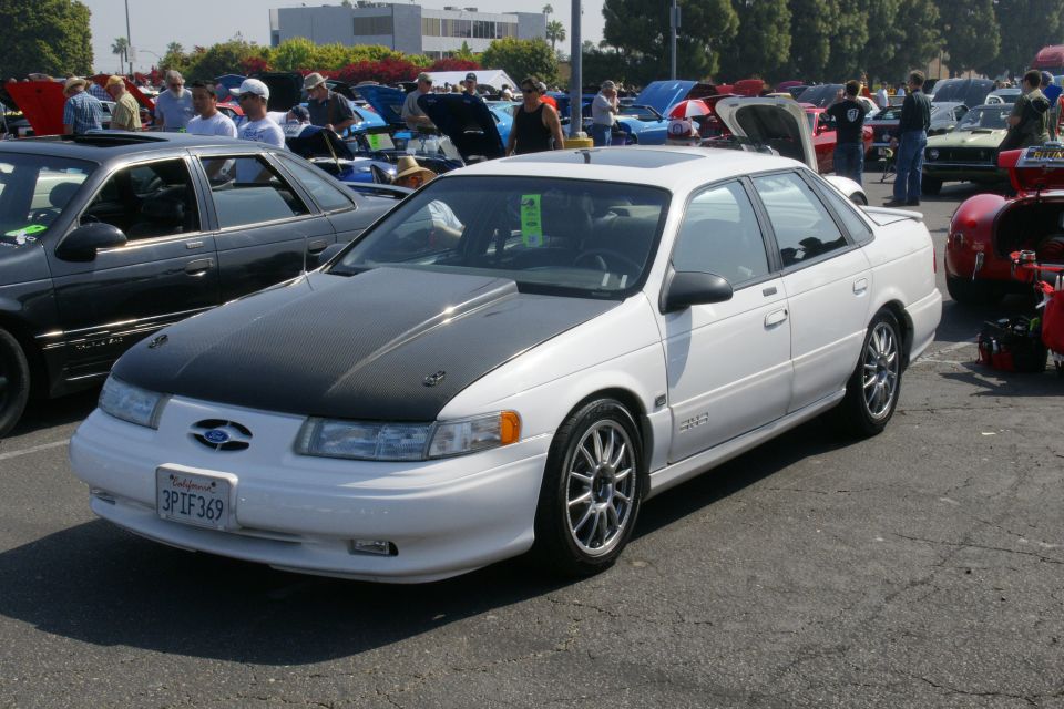 White 1992 Ford Taurus sedan with a black hood and aftermarket wheels, parked outdoors