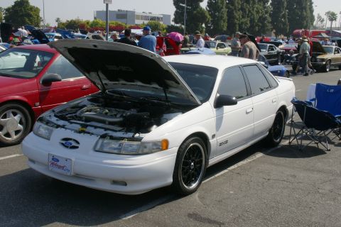 1992 Ford Taurus - A white 1992 Ford Taurus is displayed with its hood open at a car show, alongside other vehicles.