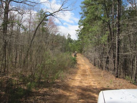 1993 Ford Bronco - Two ATVs travel down a dirt road through a wooded area, with a Supermotors logo visible in the lower right corner.
