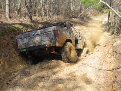 1993 Ford Bronco - This camouflaged SUV navigates a challenging muddy off-road trail, demonstrating its off-road capabilities.