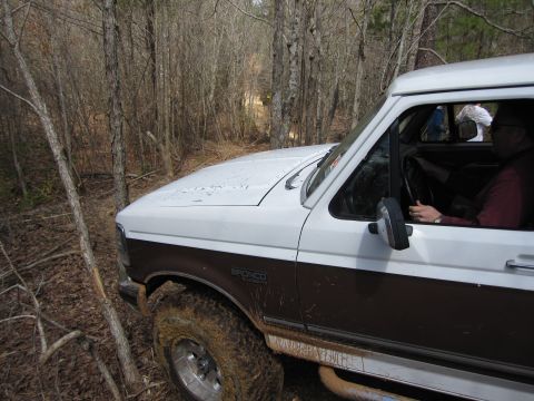 1993 Ford Bronco - Muddy 1993 Ford Bronco navigates a narrow dirt path through a forest.