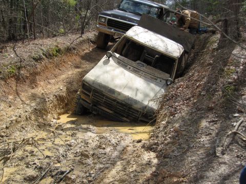 1993 Ford Bronco - Two trucks are stuck in a muddy ditch off-road, with people attempting to free them.