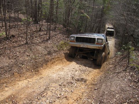 1993 Ford Bronco - Two Ford Broncos navigate a challenging off-road trail through a wooded area.
