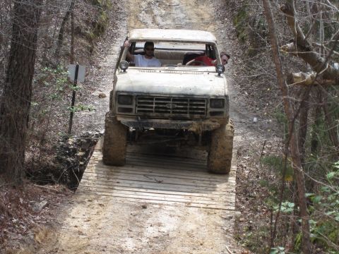 1993 Ford Bronco - This lifted truck navigates a rough trail, crossing a wooden bridge over a small ditch.