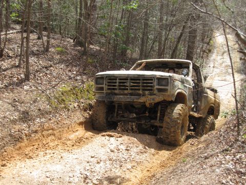 1993 Ford Bronco - A heavily modified 1980 Ford F-Series truck navigates a muddy off-road trail through a wooded area.